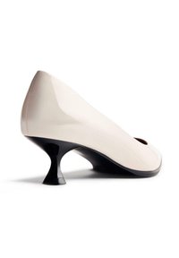 Pump in vernice beige con punta arrotondata e finitura lucida, caratterizzata da un distintivo tacco a spirale nero per un tocco di dettaglio in più.