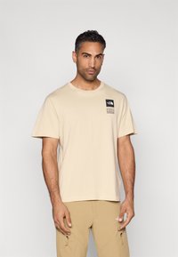 Μπεζ βαμβακερό μπλουζάκι με στρογγυλή λαιμόκοψη, κοντά μανίκια, μικρό μαύρο λογότυπο στην αριστερή πλευρά του στήθους και χαλαρή εφαρμογή.