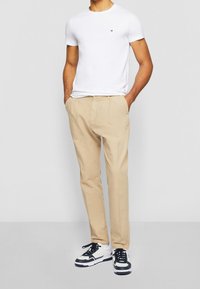 White short-sleeve t-shirt with a small logo, paired with beige trousers and black-and-white sneakers. Simple design and casual fit.