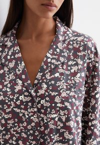 Top da pigiama con motivo floreale in tessuto grigio scuro, con colletto rotondo, tasca e chiusura a bottoni. Presenta piccoli fiori bianchi e bordeaux.