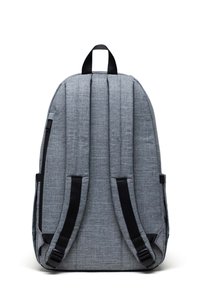 Mochila de tela gris con respaldo acolchado, correas negras ajustables y asa superior. Presenta líneas limpias y un diseño simple.