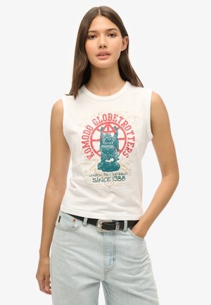 T-shirt blanche sans manches arborant un imprimé coloré avec un design de lion et du texte. Associé à un pantalon en denim bleu clair et une ceinture noire.
