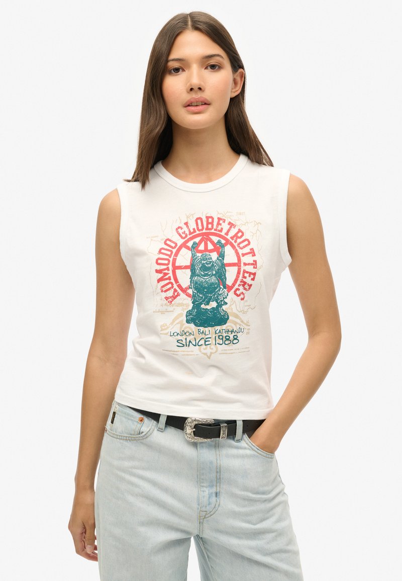 Camiseta sin mangas blanca con un estampado gráfico colorido que presenta un diseño de león y texto. Combinada con jeans de mezclilla de color azul claro y un cinturón negro.