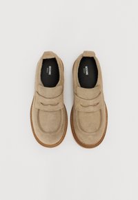 Zapatos de ante beige con dos correas anchas en la parte superior, con punta redondeada y suela de goma marrón con costuras visibles.