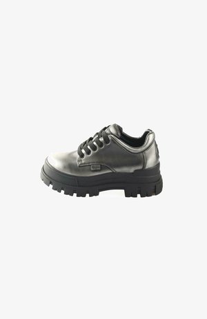 Zapato de cuero negro con puntera redondeada, suela de goma gruesa y cordones negros. Presenta un acabado liso en la parte superior y un detalle del logotipo en el costado.
