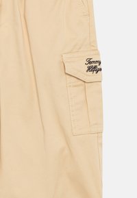 Bež kratke hlače iz bombaža s stransko žepom, ki ima črn vezenini "Tommy Hilfiger" in kontrastnimi šivi.