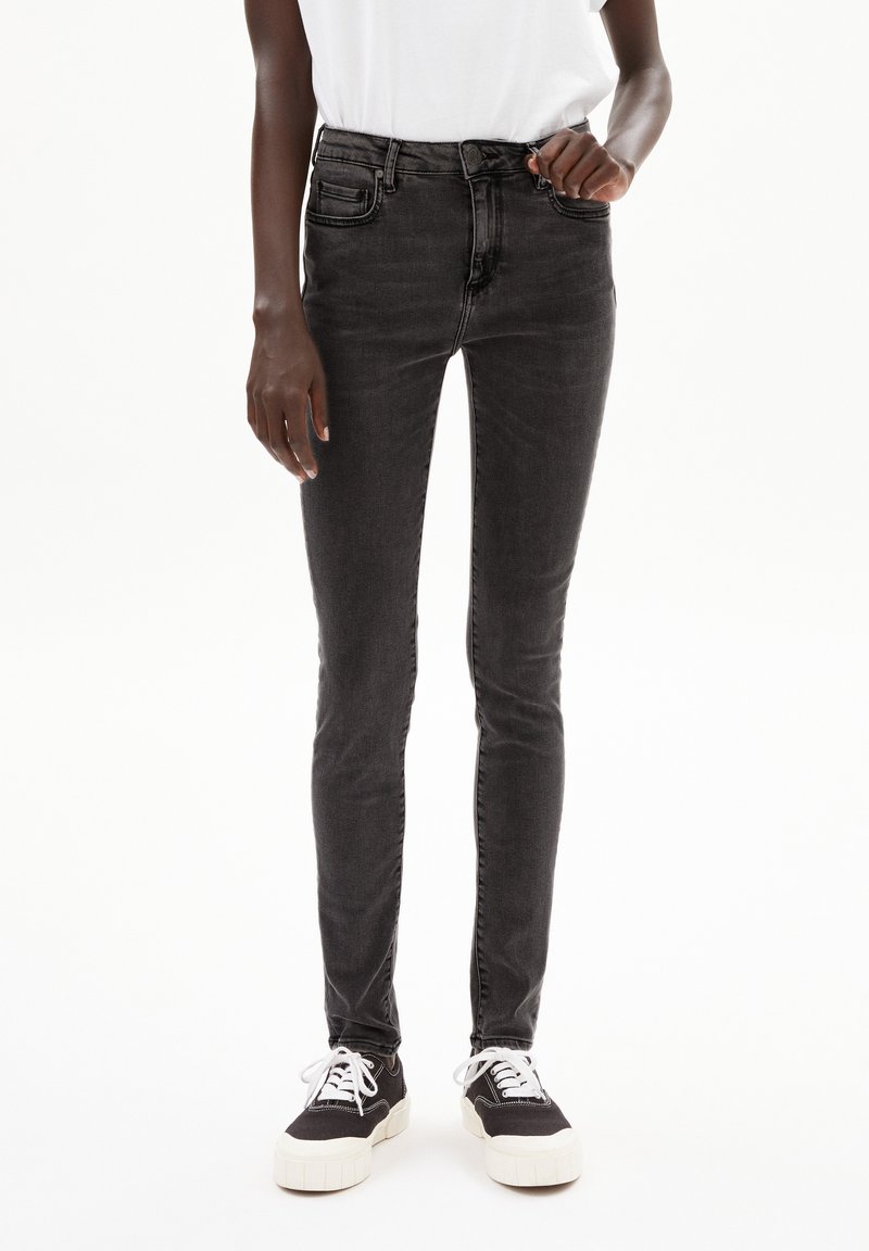 Schwarze Skinny-Jeans mit fünf Taschen, mittelschwerem Denim und einem leichten Verblassen. Kombiniert mit schwarzen Sneakern mit weißen Sohlen und Schnürsenkeln.