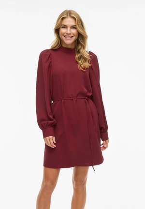 Robe bourgogne à manches longues, en tissu texturé, avec un col haut et une ceinture nouée à la taille. Elle présente des détails froncés aux épaules.