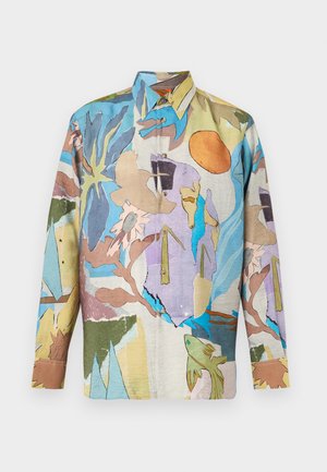 Man with short blond hair wearing a colorful abstract print button-up shirt, brown trousers, red belt, and dark brown dress shoes.