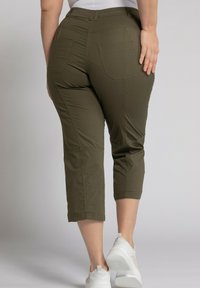 Pantalons capri vert olive avec une taille mi-haute, comportant deux poches arrière, des coutures visibles et une coupe droite. Portés avec des baskets blanches.