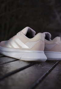 Baskets de sport rose clair avec un matériau texturé, des accents blancs, un col rembourré et une épaisse semelle blanche. Trois bandes blanches sur le côté.