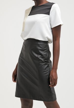 Woman wearing a short-sleeve color-blocked white, black, and beige top tucked into a high-waisted black leather knee-length skirt.