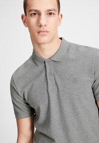 Polo gris en tissu doux, avec un col classique, une patte de boutonnage à deux boutons et un logo discret sur la poitrine.