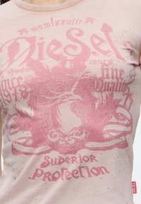 Μπεζ T-shirt Diesel με ροζ γραφικό έμβλημα αετού και κείμενο "Superior Protection" και "Since 1978", διακοσμημένο με μικρές στρας.
