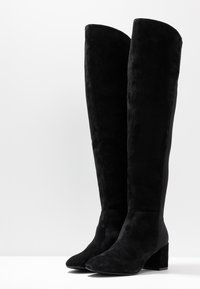 Botas negras hasta la rodilla hechas de ante texturizado, con un tacón cuadrado y una silueta elegante y ajustada con lados lisos.