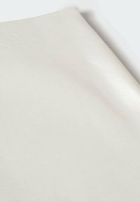 Feuille pliée de tissu en cuir synthétique lisse de couleur crème avec une texture subtile visible sur un fond blanc uni.