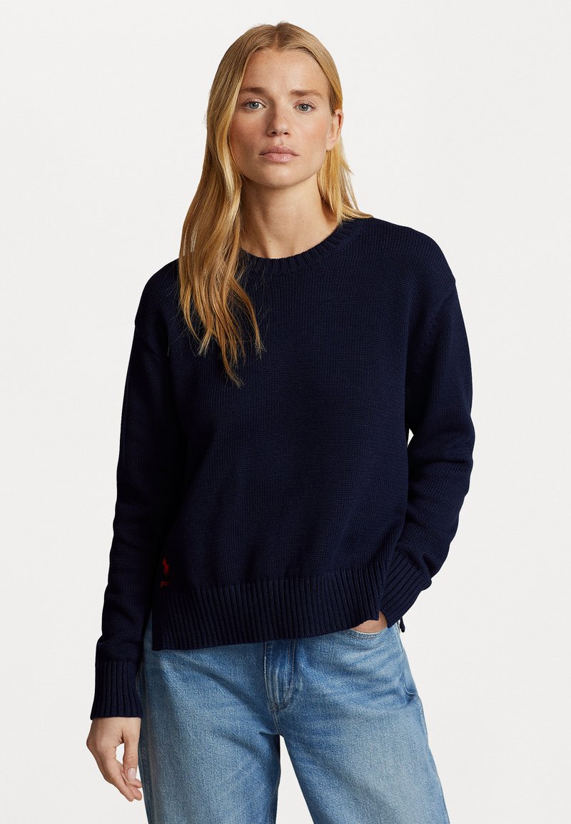 Marineblauwe gebreide trui met geribde manchetten en zoom. Voorzien van een klein rood logoaccent nabij de zoom. Casual pasvorm met een ronde halslijn.