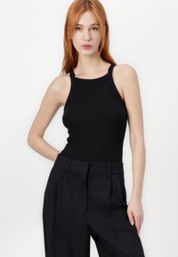 Black ribbed tank top with wide straps, round neckline, and a fitted design, paired with high-waisted black pinstripe trousers.