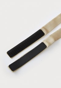 Deux sangles en tissu, l'une en satin beige avec une extrémité en velcro noir et l'autre lisse noire, toutes deux avec des bords contrastants.