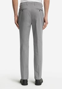 Grå byxor med rak passform, två bakfickor med knappar, skräddarsydd passform och en mjuk textur. Svarta skor bärs med byxorna.