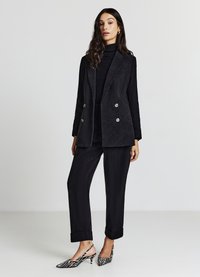 Schwarzer Cord-Blazer mit doppelseitigen silbernen Knöpfen, kombiniert mit passenden Hosen und gestreiften High-Heels. Glatte Textur und maßgeschneiderte Passform.