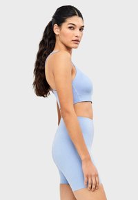 Ensemble de sport bleu clair comprenant un soutien-gorge de sport ajusté et un short taille haute. Le tissu semble lisse avec une texture subtile et sans motifs visibles.