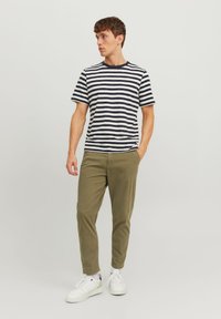 Gestreiftes T-Shirt mit navyblauen und weißen vertikalen Streifen; kombiniert mit olivgrünen, tapered Hosen und weißen Sneakers.