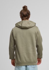 Sudadera con capucha de color verde oliva, con una textura suave, mangas largas y un corte relajado. Presenta una capucha grande y sin adornos visibles.