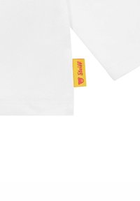Camiseta de algodón blanca de manga corta, con una etiqueta amarilla y texto rosa que dice "Steiff" y un logo de oso en la costura lateral.