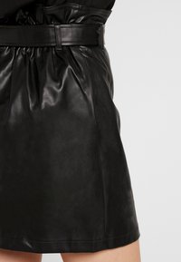 Gonna in pelle nera con vita arricciata e una cintura larga. Il tessuto ha una texture liscia e lucida ed è di taglio dritto.