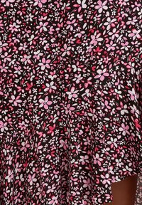 Svart tyg med ett blommönster i rosa, vitt och rött, med små blommor och blad, som faller mjukt med en lätt lyster.