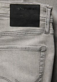 Τσέπη από ανοιχτό γκρι τζιν με μαύρη δερμάτινη ετικέτα με ανάγλυφη επιγραφή "JACK & JONES" και άλλο κείμενο εμπορικού σήματος.