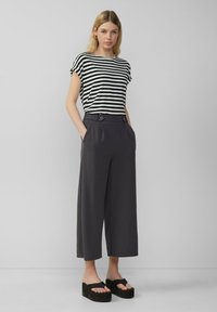 T-shirt noir et blanc à rayures avec des manches courtes, associé à un pantalon large taille haute gris foncé avec deux boutons à l'avant et des poches.