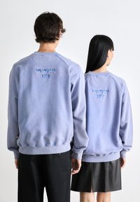Lyseblå hettegensere med brodert "MILANO EST 1978" på baksiden, paret med svarte bukser og skjørt, med ribbestrikkede mansjetter og kant.