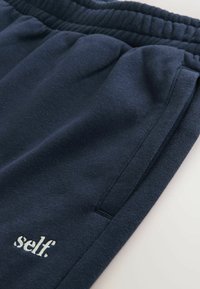 Granatowe spodnie dresowe z miękkiej bawełny, wyposażone w elastyczny pas, boczne kieszenie oraz subtelne haftowane logo "self." na mankiecie.