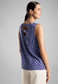 Top senza maniche in blu e bianco con motivo geometrico, caratterizzato da un dettaglio a taglio nella parte posteriore. Tessuto morbido, vestibilità rilassata.