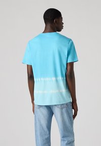 Lichtblauwe tie-dye t-shirt met een effen kleur aan de bovenkant die overgaat in een zachtere blauwe en witte gradient aan de onderkant. Korte mouwen.