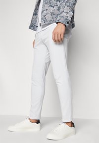 Fehér, slim fit pamut nadrág, fehér sportcipővel, fekete sarokkal, valamint egy kék virágmintás zakóval párosítva.