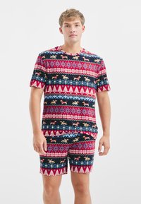 Heren twee-delig pyjama set met een marineblauwe basis, rode accenten en een feestelijk patroon van honden, bomen en sneeuwvlokken in verschillende kleuren.
