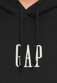 Sudadera negra con capucha y cordón, que presenta un logotipo bordado en blanco de "GAP". Textura suave y tejido duradero con un diseño minimalista.