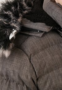 Harmaa toppatakki, jossa on teksturoitu kangas, mustat tekoturkisreunukset hupussa ja vetoketjullinen etuosan kiinnitys paksulla toppauksella.