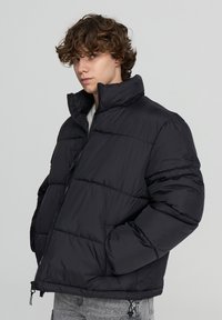 Giacca a vento nera con colletto alto, chiusura con zip e cuciture a pannello. Presenta una vestibilità rilassata e polsini elasticizzati per maggiore calore.