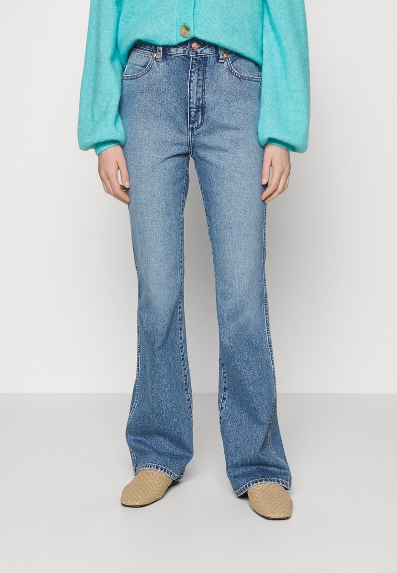 Jean bleus évasés en denim moyen, avec cinq poches, un léger effet usé et des accents de couture, associés à des chaussures à enfiler tissées beiges.