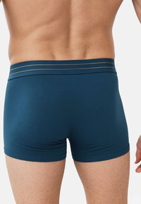 Boxerky z tmavě modré látky s hladkou texturou, s širokým pásem se třemi vodorovnými zlatými pruhy.