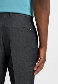 Dark gray trousers made of textured fabric, featuring a back pocket with a small accent stripe and a clean, tailored fit.