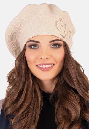 Beret tricoté beige clair avec une texture côtelée, orné de deux fleurs avec des accents en perles et d'une petite étiquette sur le côté.