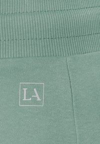 Lichtgroene katoenen blend stof met een ribbelstructuur bij de tailleband. "LA" logo in het wit binnen een vierkant aan de zijkant.