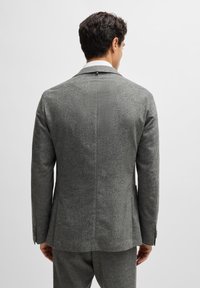 Gray wool blazer featuring a structured design, notch lapels, single back vent, and buttoned sleeves. Smooth texture and tailored fit.