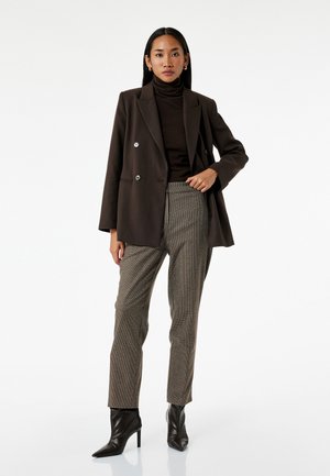 Brun dobbeltknappet blazer over en brun turtleneck og bukser med ternet mønster, parret med sorte spidse hæle støvler.