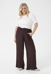 Wide-leg, dark burgundy pants with a textured finish and elastic waistband, paired with a fitted white short-sleeve top and light shoes.